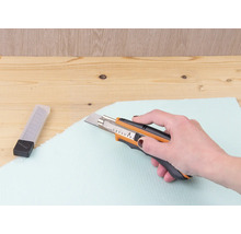 Ruka reže izolačnú dosku rezačkou.