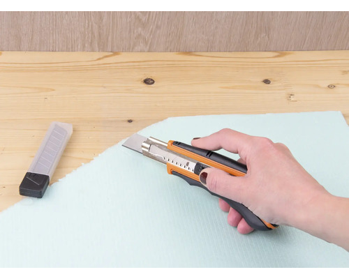 Ruka reže izolačnú dosku rezačkou.