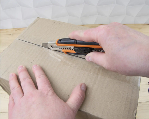 Osoba otvára kartónovú krabicu pomocou odlamovacieho noža.