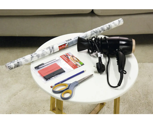 Dekoračná fólia, stierka, rezačka, nožnice, ceruzka a sušič vlasov na stole