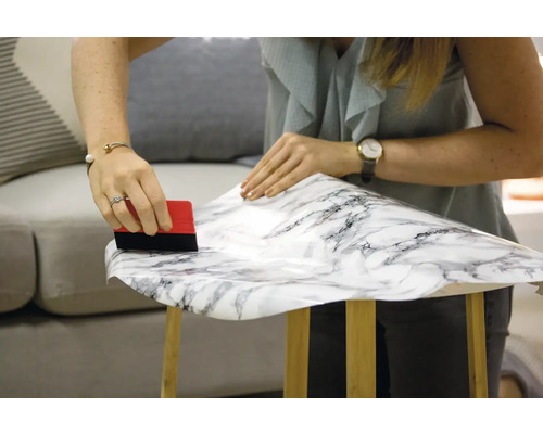 Žena nanáša dekoratívnu fóliu s mramorovým vzorom na stôl