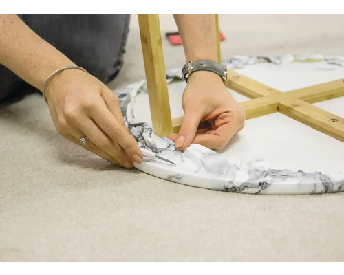 Osoba odrezáva obal z okrúhleho stola s drevenými nohami.