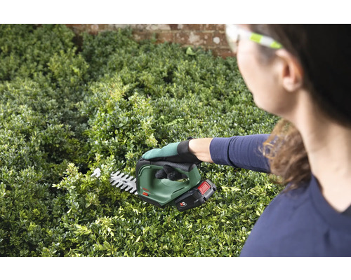 Žena strihá živý plot akumulátorovými nožnicami na živý plot