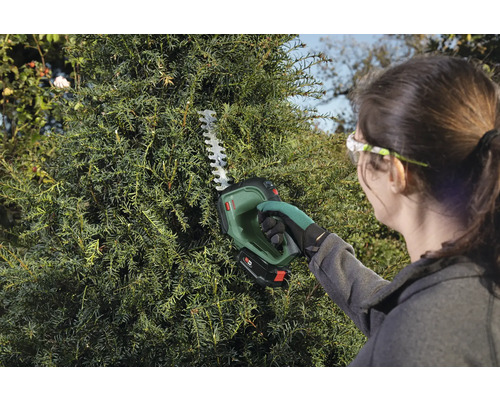 Žena strihá živý plot pomocou akumulátorových nožníc na živý plot