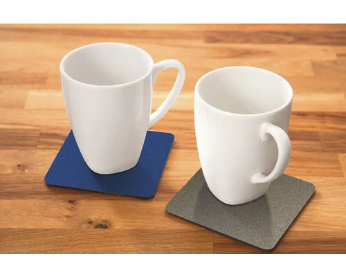 Dva biele hrnčeky na podložkách na drevenom stole.