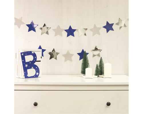 Dekoratívna scéna s hviezdnou girlandou, ozdobným písmenom, vianočnými stromčekmi a sviečkami na komode