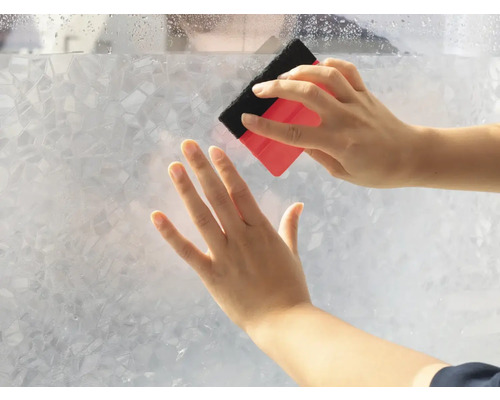 Osoba nanáša fóliu na ochranu súkromia stierkou na sklenenú tabuľu