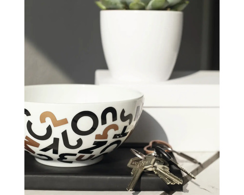 Dekoratívna misa s motívom písmen, izbová rastlina v bielom kvetináči a zväzok kľúčov na polici.