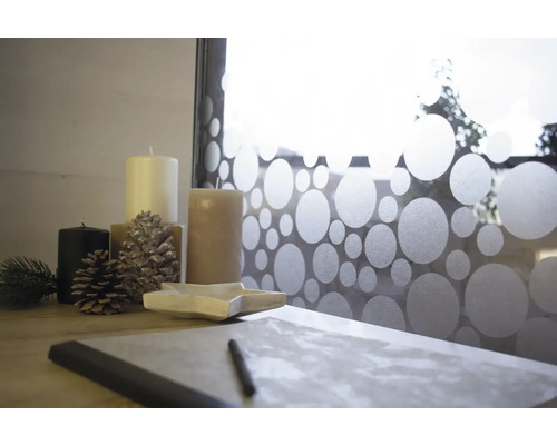 Dekoratívne usporiadanie so sviečkami, šiškami, miskou v tvare hviezdy a písacími potrebami pred oknom s bodkovaným vzorom.