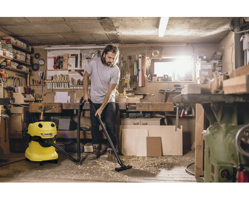 Muž vysáva dielňu žltým viacúčelovým vysávačom Kärcher.