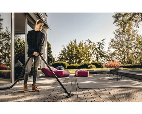 Žena čistí drevenú terasu vonkajším vysávačom.