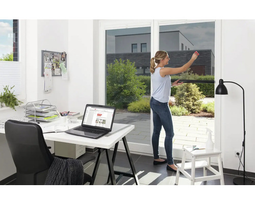 Žena aplikuje protislnečnú fóliu na okno, v pozadí kancelária