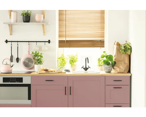 Svetlá kuchyňa s ružovými skrinkami, drevenou pracovnou doskou a kuchynským náčiním