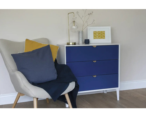 Obývacia izba so stoličkou, vankúšmi, dekou a komodou s tromi zásuvkami