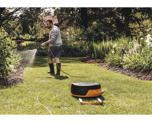 Muž zavlažuje záhradnou hadicou trávnik vedľa bubna na hadicu.