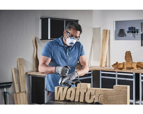 Muž pracuje s drevoobrábacou frézou na kuse dreva s nápisom Wolfer, pričom má na sebe ochrannú masku a ochranné okuliare v dielni.