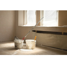 Miestnosť s vedrami farby, valčekom a krycou fóliou na renováciu