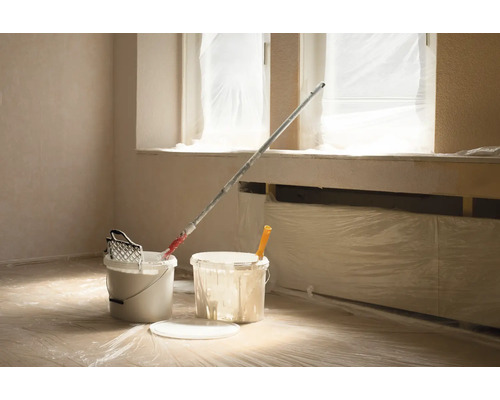 Miestnosť s vedrami farby, valčekom a krycou fóliou na renováciu