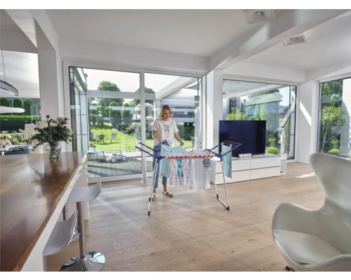 Žena vešia bielizeň na sušiak v jasnej obývačke.