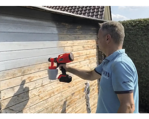 Muž natiera drevenú stenu farbou pomocou striekacieho systému