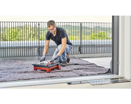 Muž reže dlaždice rezačkou dlaždíc na balkóne.