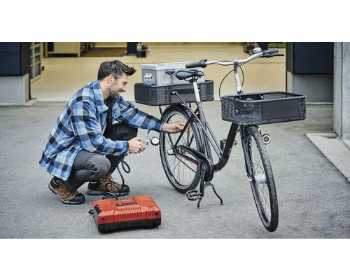 Muž pumpuje pneumatiku bicykla pomocou kompresora. Bicykel má košíky a nosič.