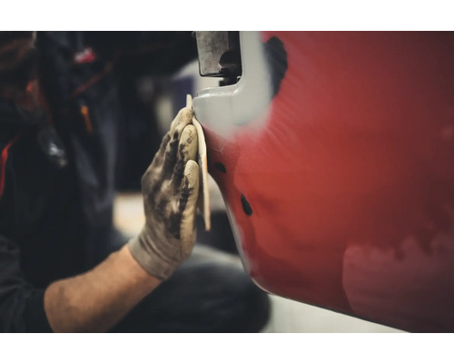 Osoba brúsi červené vozidlo brúsnym papierom.