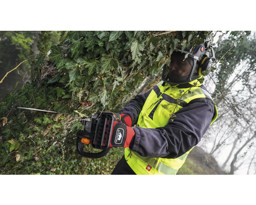 Osoba s ochranným vybavením reže konáre a brečtan tyčovou motorovou pílou.