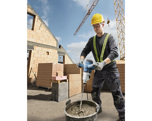 Stavebný robotník mieša maltu s elektrickým miešadlom na stavenisku.