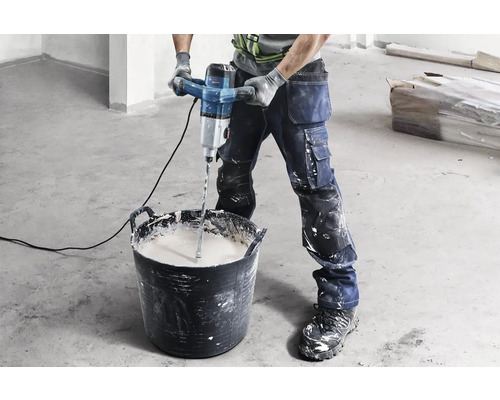 Remeselník mieša maltu elektrickým miešadlom vo vedre.