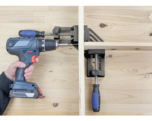 Osoba skrutkuje akumulátorovým skrutkovačom obrobok, ktorý je upevnený pomocou rohového zveráka.