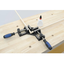 Rohová svorka drží dva kusy dreva v uhle 90 stupňov na pracovnom stole.