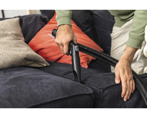 Osoba čistí pohovku pomocou hubice vysávača