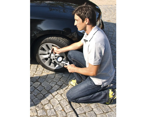 Muž hustí pneumatiku automobilu pomocou merača tlaku v pneumatikách.