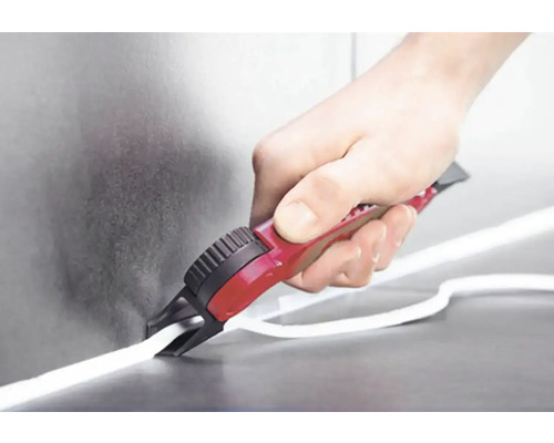 Osoba reže biele tesnenie rezačkou škár. Nástroj má červenú rukoväť.