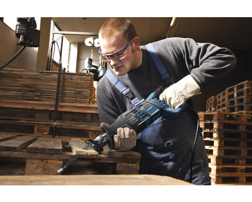 Muž pília drevenú dosku priamočiarou pílou.