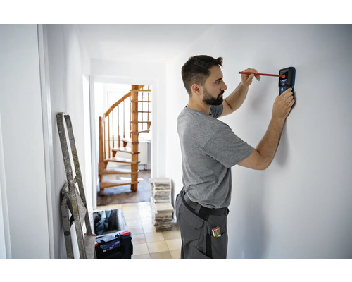 Muž používa detektor na nájdenie objektov v stene v dome.