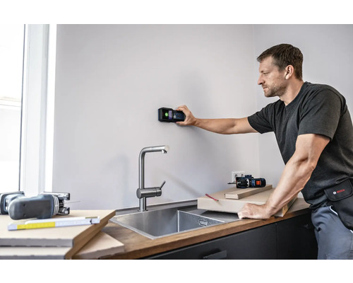 Muž používa digitálny detektor na stene v kuchyni.