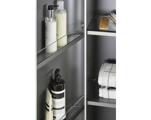 Detailný pohľad na kúpeľňovú skrinku so sklenenými policami a rôznymi kúpeľňovými potrebami, ako sú uteráky, kefy a produkty starostlivosti.