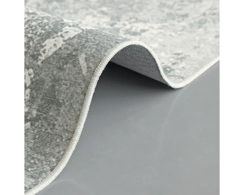 Detailný pohľad na sivý koberec s abstraktným vzorom a obšitými okrajmi