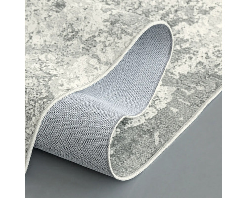 Sivý koberec s abstraktným vzorom, čiastočne zrolovaný, aby ukázal zadnú stranu