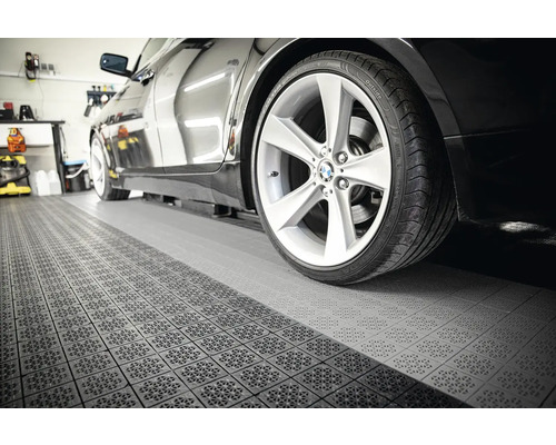 Čierne auto na podlahe garáže s dlaždicovou štruktúrou.