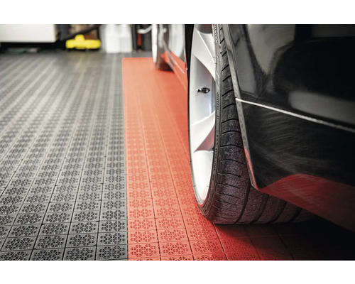 Detailný záber čierneho auta na garážových dlaždiciach v sivej a červenej farbe.