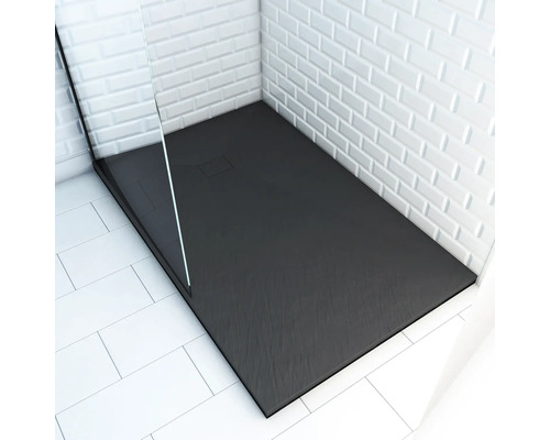 Sprchovací kút v úrovni podlahy s obdĺžnikovou, tmavou sprchovacou vaničkou a sklenenou sprchovacou zástenou pred stenou s bielymi dlaždicami.