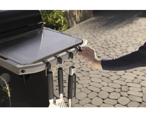 Detailný záber grilovacieho stola s grilovacím náčiním na hákoch.