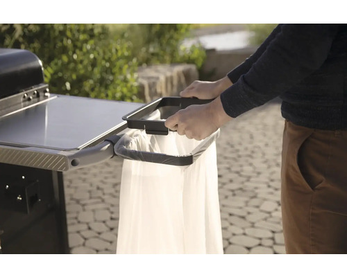 Osoba pripevňuje vrece na odpadky ku grilovaciemu vozíku pre čisté a praktické grilovanie.