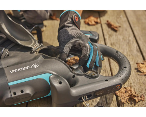 Akumulátorový vysávač lístia Gardena s otvorenou klapkou a rukou v záhradnej rukavici, ktorá odstraňuje lístie