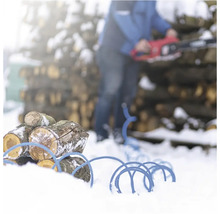 Hromada dreva s modrým káblovým bubnom v snehu a osoba s motorovou pílou v pozadí