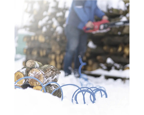 Hromada dreva s modrým káblovým bubnom v snehu a osoba s motorovou pílou v pozadí