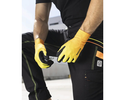 Osoba v pracovných nohaviciach a pracovných rukaviciach drží skrutku.